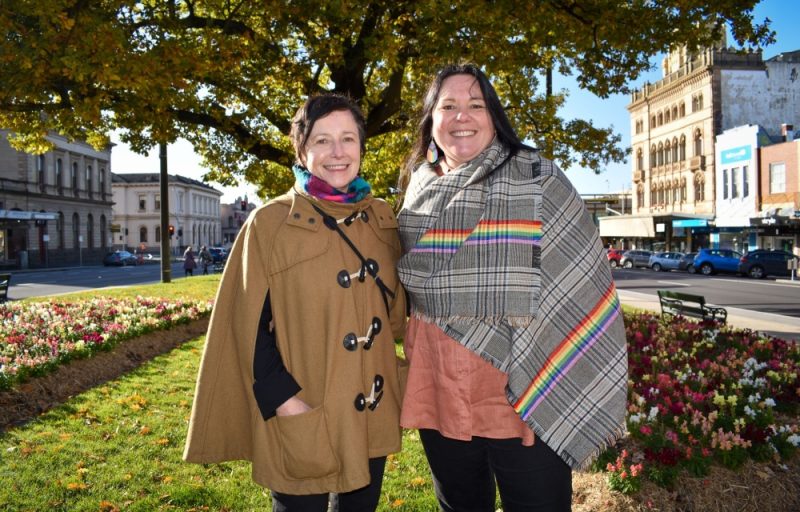 Two women smiling in a park with flowers.