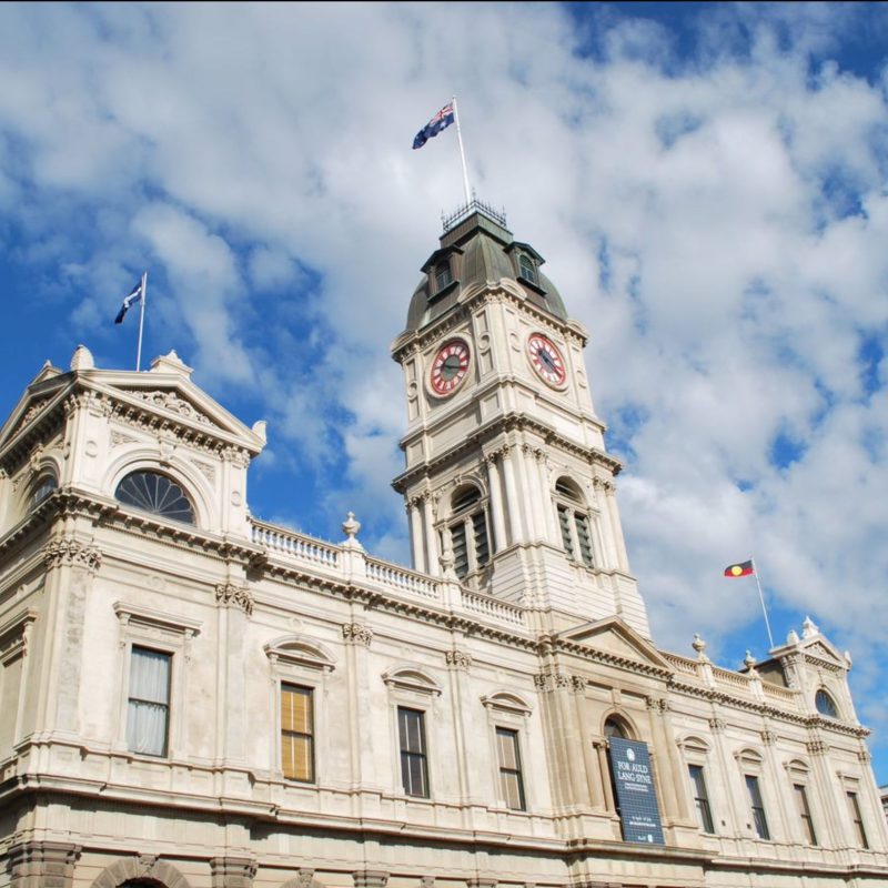 Historic clock tower with Australian flags on building.