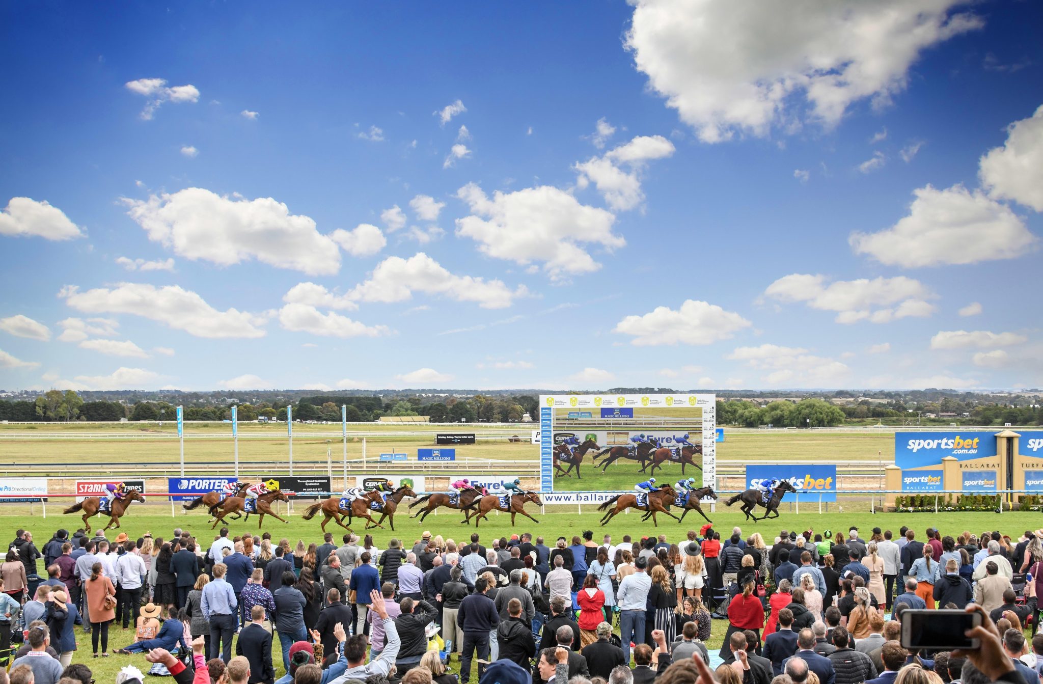 Crowd watching horse race on a sunny day.