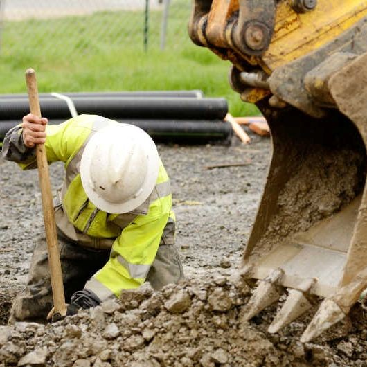 Construction worker digging beside excavator on site.