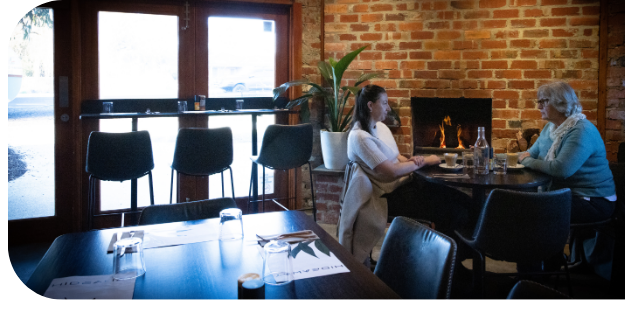 Two women dining in cosy restaurant with fireplace.
