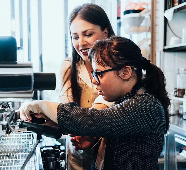 Woman helping barista with espresso machine.